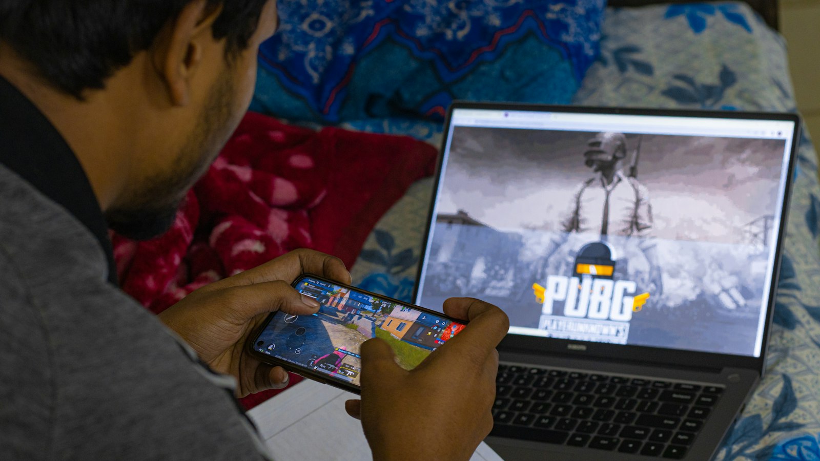 A person playing a mobile game on a smartphone beside a laptop screen